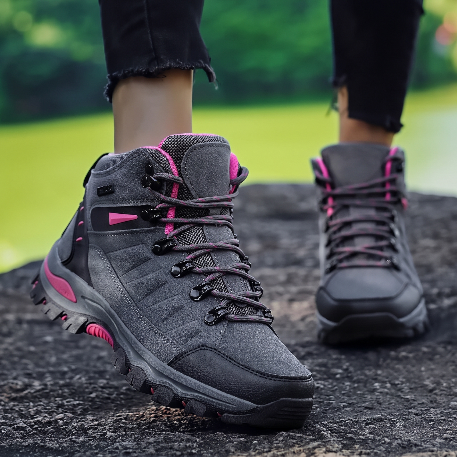 Frau trägt graue wasserdichte Wanderschuhe mit pinken Akzenten beim Gehen auf einem Felsen am See