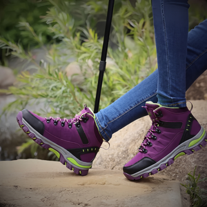 Frau trägt violette wasserdichte Wanderschuhe mit neongrünen Akzenten beim Wandern mit Trekkingstock